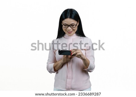 Young smiling asian nerdy woman watching a video on her smartphone. Isolated on white background.