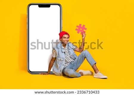 Full length photo of sweet cute man wear jeans outfit holding hash tag device empty space isolated yellow color background