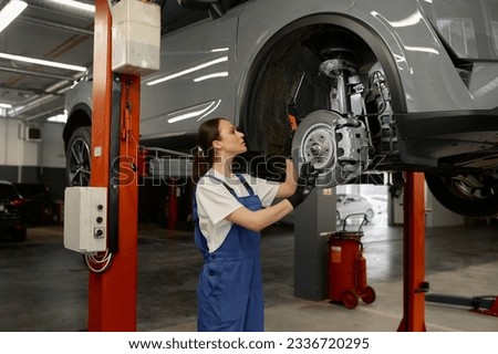 Woman mechanic fixing wheel hub or disc brake of raised car on lift mechanism Royalty-Free Stock Photo #2336720295