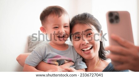 Authentic shot of Mother taking photo or video, cute Asian baby boy with mobile phone at home, happy smile face. Little kid innocent adorable. Technology lifestyle parenthood concept.