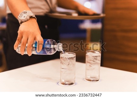 Waiter hand pouring water from bottel into a glass in restaurant. Royalty-Free Stock Photo #2336732447