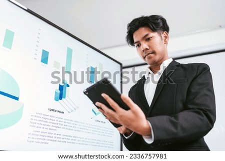Portrait of a smart Asian young entrepreneur man using his digital tablet while standing in the office. A businessman wearing a suit looks on the tablet while using it with a smile.