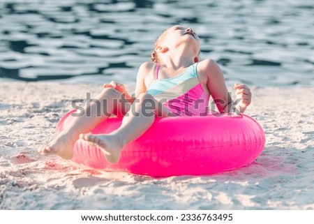 Happy joyful child girl in swimsuit having fun with swimming ring on a sand beach. Summer beach concept