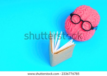 Human brain in nerdy glasses reads a book isolated on blue background with copy space. Education and learning related concept.