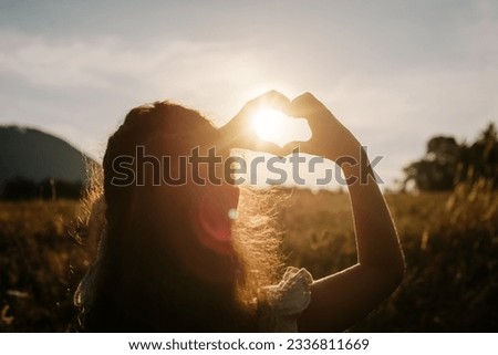 Back view of little girl child making heart with hands during calm sunset or sunrise at warm summer day. Sunbeams Sunlight. Happy Valentines day, Mothers Day, love nature or life happiness concept