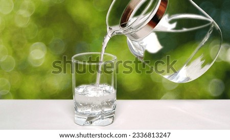 Pouring  fresh, mineral, drinking water from the jug into a glass, on a bokeh bubble background  Royalty-Free Stock Photo #2336813247