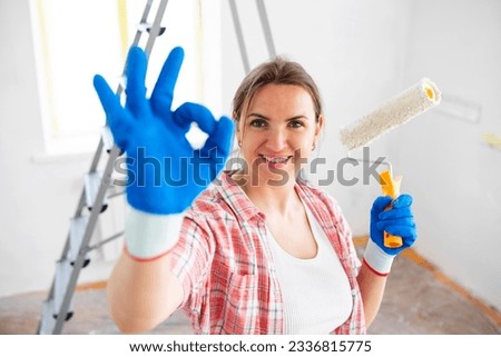 Woman holding roller painter doing ok sign while doing repair in room