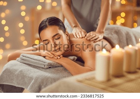 Young woman having back massage in beauty spa salon. Serene beautiful relaxed woman lying on couch with closed eyes receiving and enjoying relaxing massage. Beauty treatment, body care Royalty-Free Stock Photo #2336817525