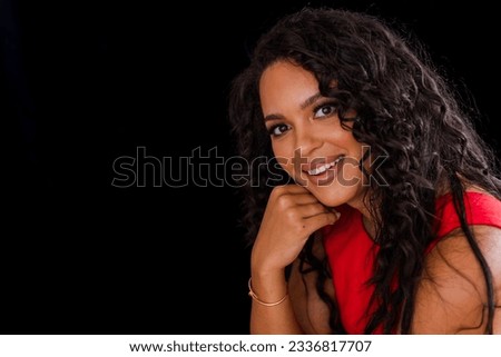 Young multi ethnic female with long dark curly hair in red outfit in front of black background