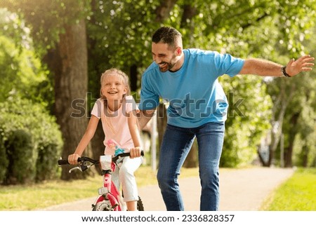 Outdoors activities. Happy father teaching his child daughter to ride a bike in the park, enjoying time together on weekend on nature. First bike ride Royalty-Free Stock Photo #2336828357