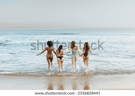 Back view of group of diverse female friends splashing water while running together at the beach, young women having fun and enjoying their summer time