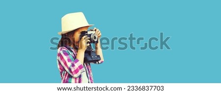 Portrait of child with film camera taking picture wearing summer straw hat on blue background, blank copy space for advertising text