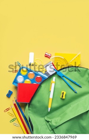 Top view of school backpack and school supplies with space for text over yellow background. Back to school concept