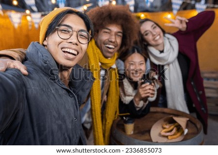 Diverse group of young people taking selfie portrait with cell phone enjoying winter holidays together