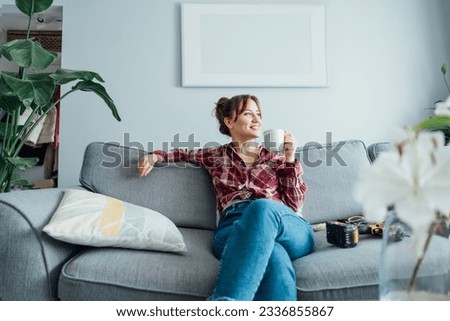 Happy smiling proud of herself young woman relaxing with coffee cup after she puts by her own a picture on the wall at her home. Housekeeping work. Doing repair herself. DIY, gender equality concept.