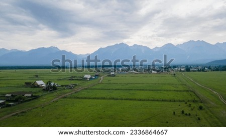 Aerial view of the meadows with cows and horses near to the high mountain ridge and country road at summer cloud rain day, blue color of the picture
