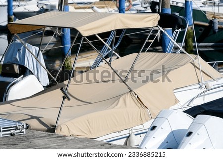 Partial shot close up of beige foldable roof sun shade bikini bimini top sun sail canopy and sport boat motor boat covered with brown canvas in a harbor as a concept for protection from sun wind Royalty-Free Stock Photo #2336885215
