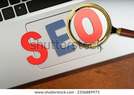 Magnifying glass magnifying wooden letters stands for SEO abbreviation lying on laptop at desk (Search Engine Optimization) Top view on wooden table with blocks. Top view. Close up.