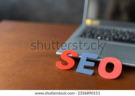 Wooden letter stands for SEO abbreviation lying on laptop at desk. Modern marketing buzzword SEO - Search engine optimisation. Top view on wooden table with blocks. Top view. Close up.