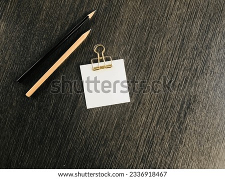 black and brown pencils and white notepaper with golden clipper are put on the dark brown desk with copy space on the right side of the frame