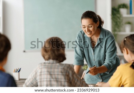Happy kids and teacher at school. Woman and children are talking in the class. Royalty-Free Stock Photo #2336929013