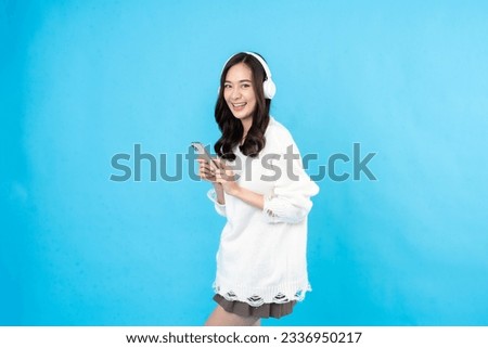 long haired asian woman Listen to music with white wireless headphones via smartphone. a happy holiday Wear a coat and a skirt. Take a photo of the blue scene in the studio.