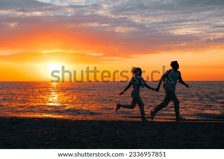 Silhouette of happy young couple in love together holding hands and running along seashore at sunset, copy space. Romance, relationship, date, valentine's day concept. Royalty-Free Stock Photo #2336957851