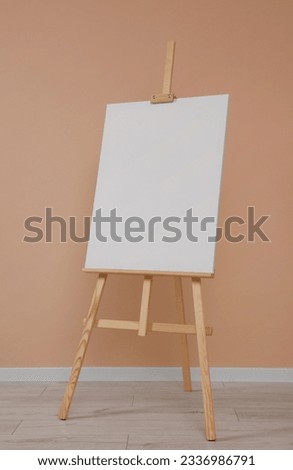 Wooden easel with blank canvas near beige wall indoors