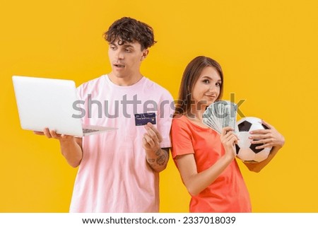 Young couple with soccer ball, laptop and money on yellow background. Sports bet concept