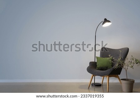 Glowing lamp, grey armchair with cushion and houseplant near grey wall Royalty-Free Stock Photo #2337019355