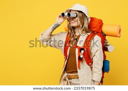 Side view young happy woman carry backpack with stuff mat using binocular isolated on plain yellow background. Tourist leads active lifestyle walk on spare time. Hiking trek rest travel trip concept Royalty-Free Stock Photo #2337019875