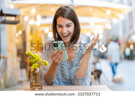 Pretty young woman use mobile smartphone celebrating win good message news, lottery jackpot victory, giveaway online outdoors. Happy girl tourist walking iin urban city cafe terrace. Town lifestyles Royalty-Free Stock Photo #2337037713
