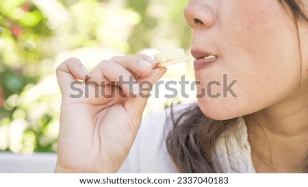 A woman in white is eating biscuit with sliced cheese in the morning with bokeh garden backgrounds. Concept for Breakfast, Relaxation, Leisure activity, Snacking Habbit, Diet, and Healthy Life Style.