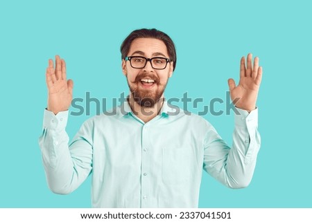 Happy joyful young man in shirt and glasses holding hands apart to show how huge something is. Funny cheerful excited nerd student on blue background telling and boasting about object of very big size