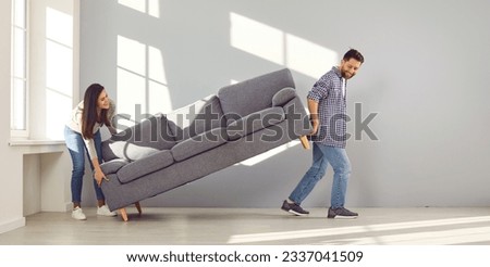 Happy couple placing sofa in living room of new home. Smiling husband and wife carrying couch in empty living room. Family moving in new apartment or remodeling home Royalty-Free Stock Photo #2337041509