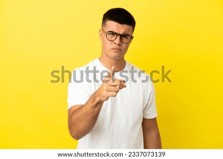 Young handsome man over isolated yellow background frustrated and pointing to the front