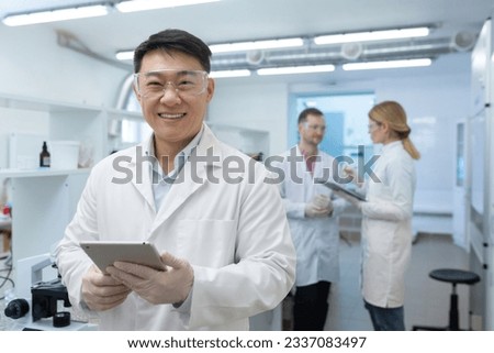 Portrait of an Asian laboratory technician scientist inside a laboratory, the man is looking at the camera and smiling, the scientist is working with colleaguesmanufacturing biological supplements.