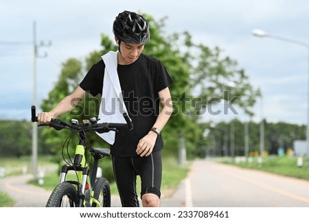 Young asian male cyclist with injured knee carry bicycle walk in park after an accident