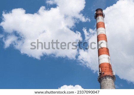 A high red-white chimney of a boiler room against a blue sky with clouds. Air pollution. City heating. Industrial zone. Place for text