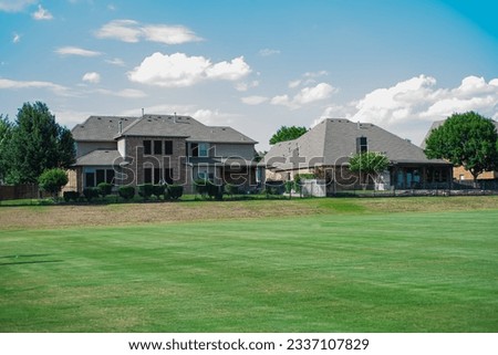 Large grassy and rolling lawn of suburban park next to upscale residential neighborhood row of two-story houses in Flower Mound, Texas, USA. New development homes with metal fence solar roof panels Royalty-Free Stock Photo #2337107829