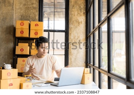 Asian male new business owner selling online at home with packaged goods for sale among many boxes with parcels on the back with independent start-ups and home offices of SMEs delivering goods.