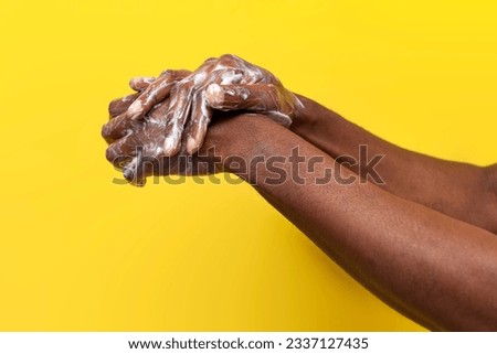 hands of African American man in soap and foam on yellow isolated background, the guy washes his hands in white cream, close-up