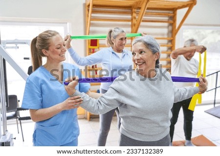 Smiling female therapist assisting elderly woman doing workout with resistance band at rehab center Royalty-Free Stock Photo #2337132389