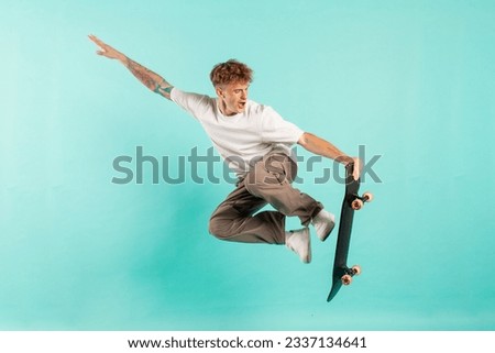young crazy guy rides skateboard and jumps on blue isolated background, hipster in sunglasses flies with skateboard in the air and does extreme trick