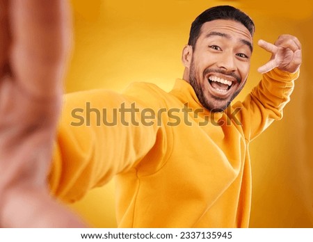 Peace sign, selfie and happy portrait of a man in studio with a hand, emoji and a smile. Male asian fashion model excited on a yellow background with a positive icon for social media profile picture