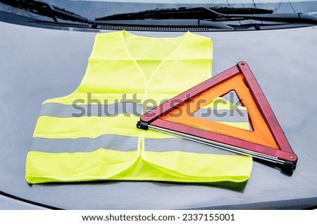 yellow reflective vest and warning triangle lie on hood of car. Safety on road in case of breakdown Royalty-Free Stock Photo #2337155001