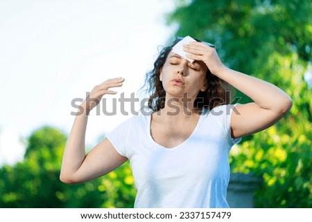 Young woman having hot flash and sweating in a warm summer day. Woman drying with paper napkin in too hot weather Royalty-Free Stock Photo #2337157479