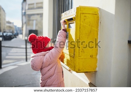 Adorable preschooler girl putting letter in yellow post box on a street of Paris, France Royalty-Free Stock Photo #2337157857