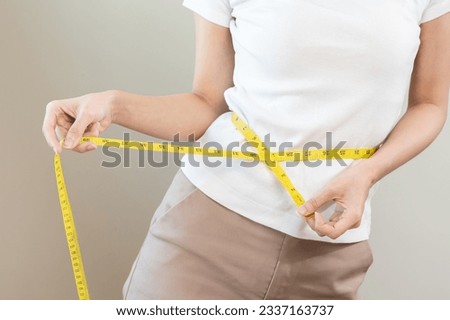 Diet, slim shape asian young woman standing, hand using measure tape around waist, body. Happy, pleasure girl slim slender on white background. Diet session for wellbeing health, eat good food people. Royalty-Free Stock Photo #2337163737