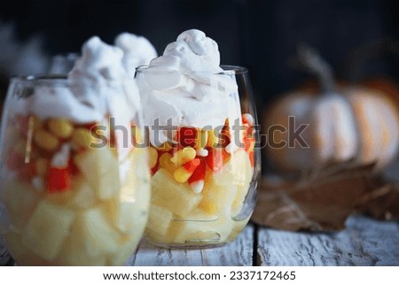 Halloween parfait made from layers of chopped pineapples, candy corn, and whipped cream. Selective focus with pumpkins and leaves in  blurred background.  